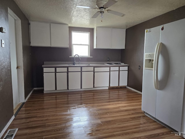 kitchen with white refrigerator with ice dispenser, visible vents, dark wood finished floors, white cabinets, and a sink