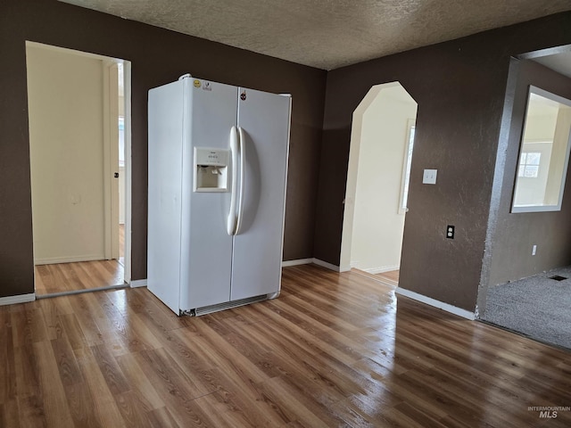 kitchen featuring a textured ceiling, white refrigerator with ice dispenser, wood finished floors, and baseboards