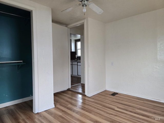 unfurnished bedroom featuring a closet, ceiling fan, a sink, wood finished floors, and baseboards