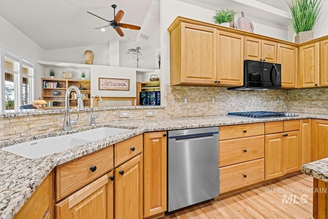 kitchen featuring appliances with stainless steel finishes, a sink, lofted ceiling, light wood finished floors, and light stone countertops