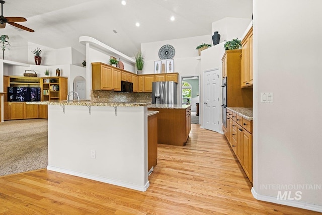 kitchen with stainless steel appliances, a breakfast bar, ceiling fan, a peninsula, and light wood finished floors