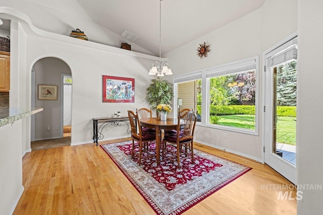 dining area with a chandelier, lofted ceiling, arched walkways, light wood finished floors, and baseboards