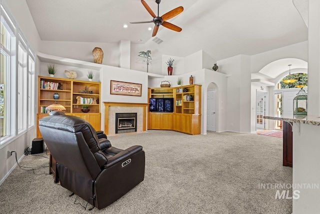 carpeted living room featuring arched walkways, a ceiling fan, healthy amount of natural light, a tile fireplace, and high vaulted ceiling