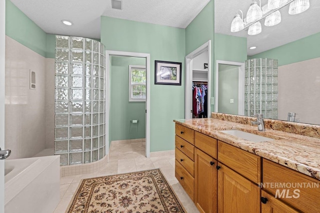 bathroom with walk in shower, a garden tub, vanity, a walk in closet, and tile patterned flooring