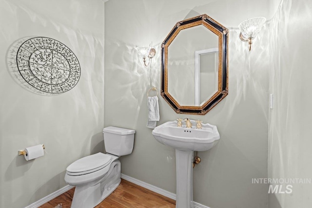 half bathroom featuring toilet, wood finished floors, baseboards, and a sink