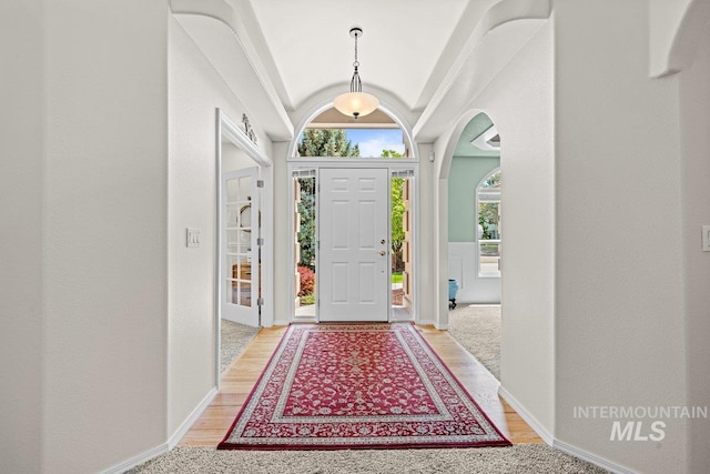 foyer with vaulted ceiling, light wood-style flooring, arched walkways, and baseboards