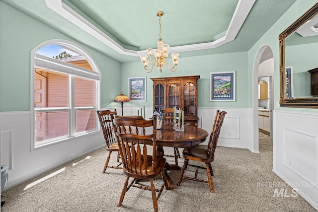 dining area featuring arched walkways, a raised ceiling, a chandelier, carpet floors, and a textured ceiling