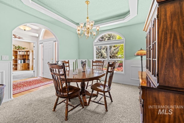 dining area featuring arched walkways, a raised ceiling, a chandelier, a wainscoted wall, and a textured ceiling