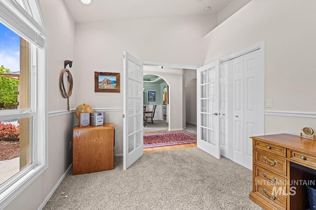 hallway featuring french doors, arched walkways, carpet, and high vaulted ceiling