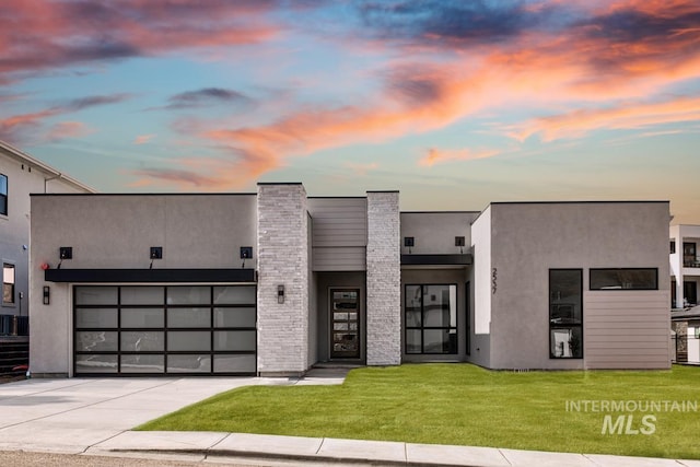 contemporary house featuring an attached garage, driveway, stone siding, stucco siding, and a front lawn