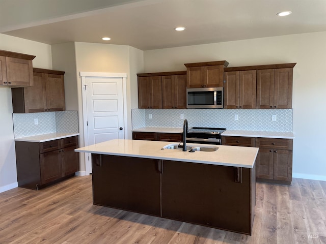 kitchen with light countertops, stainless steel microwave, light wood-style floors, a sink, and an island with sink