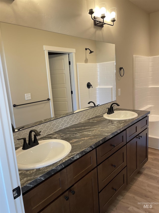 full bathroom featuring double vanity, wood finished floors, a sink, and tiled shower