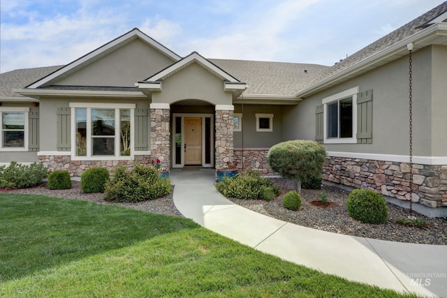 view of front facade with stone siding, roof with shingles, a front yard, and stucco siding
