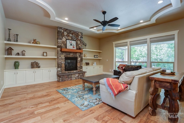 living area with light wood-style floors, ceiling fan, a tray ceiling, a fireplace, and recessed lighting