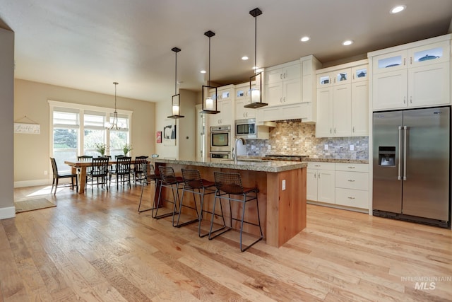 kitchen with tasteful backsplash, a breakfast bar area, light wood-style flooring, white cabinets, and appliances with stainless steel finishes
