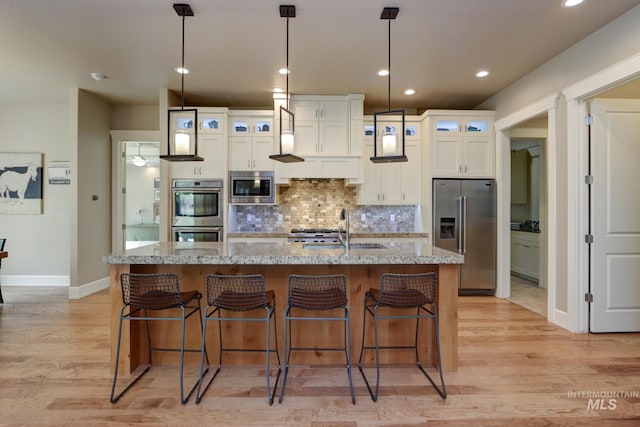kitchen with white cabinets, stainless steel appliances, a sink, and a center island with sink