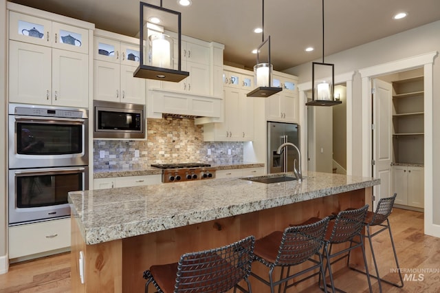 kitchen with decorative backsplash, stainless steel appliances, a sink, and light wood finished floors