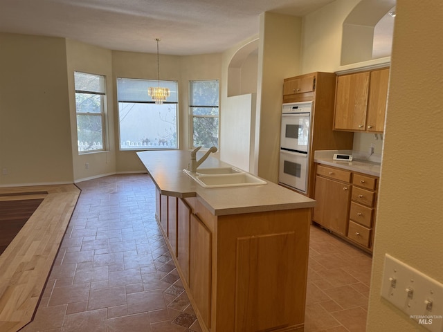 kitchen with a chandelier, an island with sink, double oven, sink, and decorative light fixtures