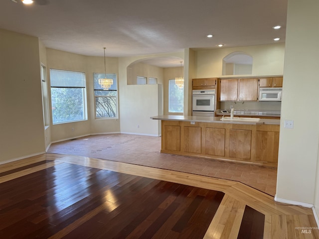 kitchen featuring white appliances, hardwood / wood-style flooring, hanging light fixtures, a notable chandelier, and sink