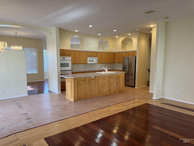 kitchen featuring sink, white appliances, an island with sink, pendant lighting, and a notable chandelier