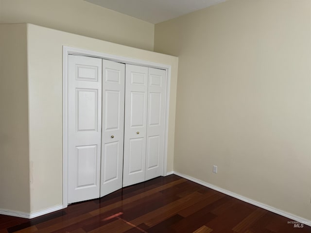 unfurnished bedroom with dark wood-type flooring and a closet