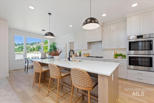 kitchen with tasteful backsplash, a sink, light wood-style floors, gas cooktop, and stainless steel double oven