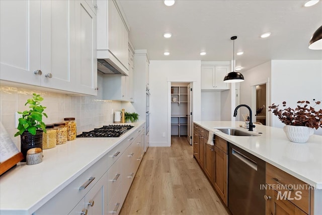 kitchen featuring white cabinetry, stainless steel appliances, light wood-style floors, and a sink