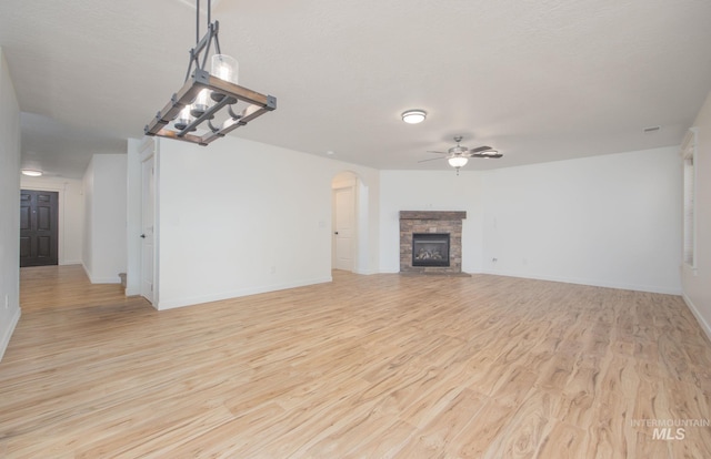 12476 W Kempshire Ct, Star, ID 83669 - unfurnished living room with ceiling fan, a fireplace, light wood-style flooring, and arched walkways
