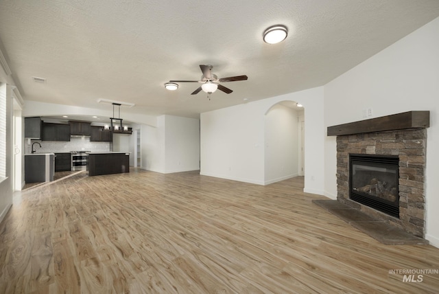 12476 W Kempshire Ct, Star, ID 83669 - unfurnished living room with ceiling fan, a stone fireplace, light wood-style flooring, a textured ceiling, and arched walkways