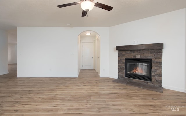 12476 W Kempshire Ct, Star, ID 83669 - unfurnished living room with wood finished floors, ceiling fan, arched walkways, and a stone fireplace