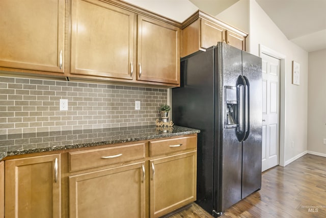 kitchen with dark stone countertops, wood finished floors, baseboards, backsplash, and black refrigerator with ice dispenser