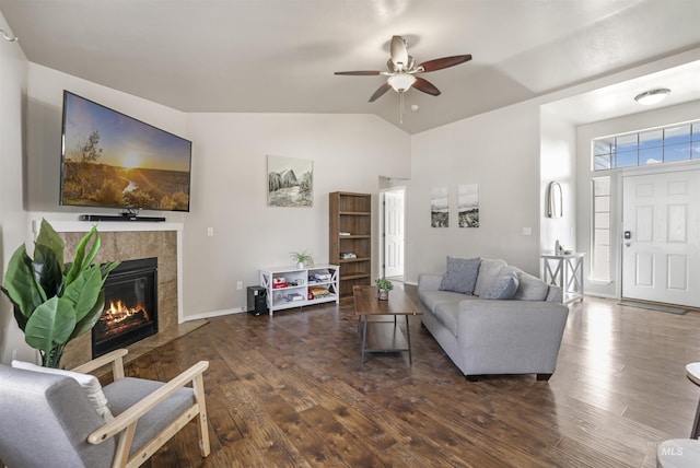 living room with ceiling fan, vaulted ceiling, a tiled fireplace, and hardwood / wood-style flooring