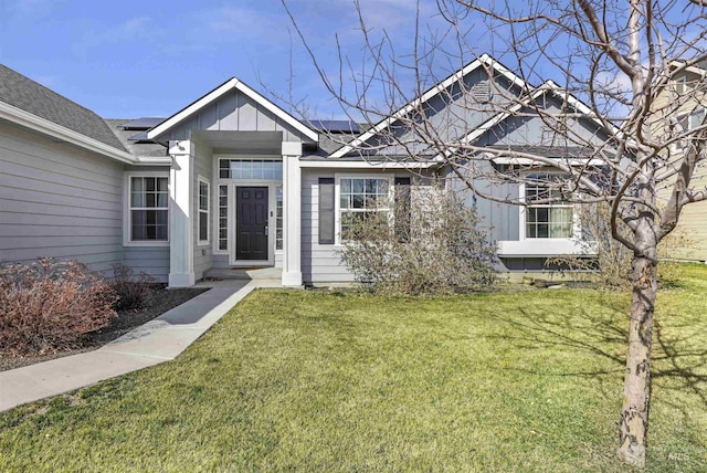 ranch-style house with roof mounted solar panels, board and batten siding, and a front lawn