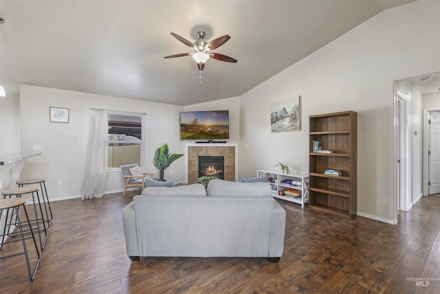 living area featuring a ceiling fan, baseboards, dark wood finished floors, lofted ceiling, and a tile fireplace