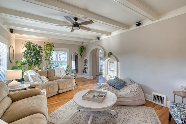 living room featuring arched walkways, light wood finished floors, visible vents, beamed ceiling, and baseboards