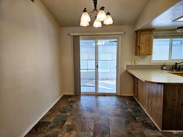 interior space featuring sink, a notable chandelier, a textured ceiling, decorative light fixtures, and kitchen peninsula