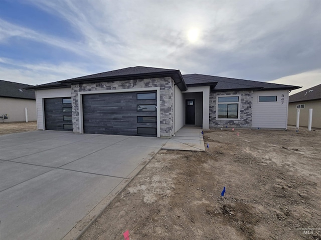 prairie-style home with an attached garage, driveway, and stone siding