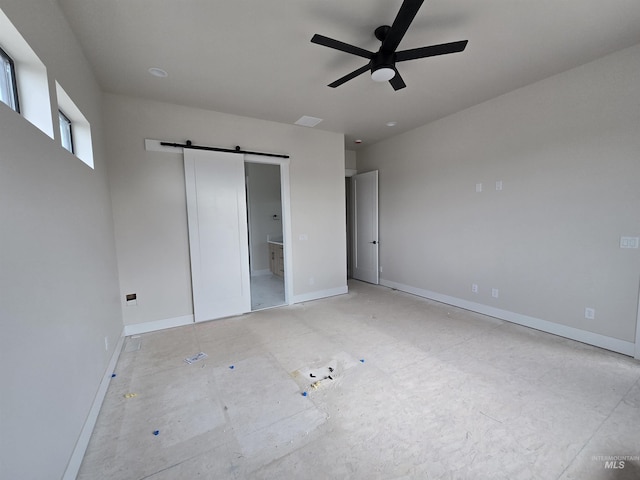 unfurnished bedroom featuring a barn door, baseboards, connected bathroom, and a ceiling fan