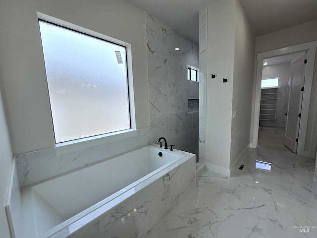 full bathroom featuring marble tiled floors, a marble finish shower, a garden tub, and baseboards