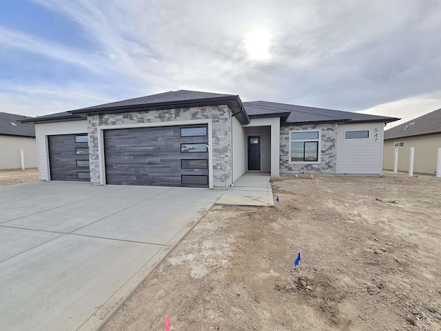 prairie-style home with a garage, stone siding, and driveway