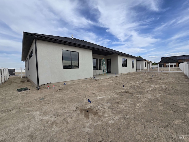 rear view of property featuring stucco siding, fence, and a patio area