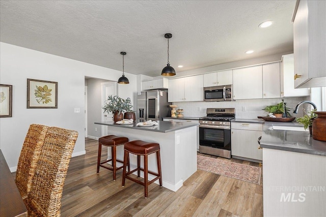 4849 N Willowside Ave, Meridian, ID 83646 - kitchen with appliances with stainless steel finishes, dark countertops, light wood-style flooring, decorative backsplash, and a breakfast bar area