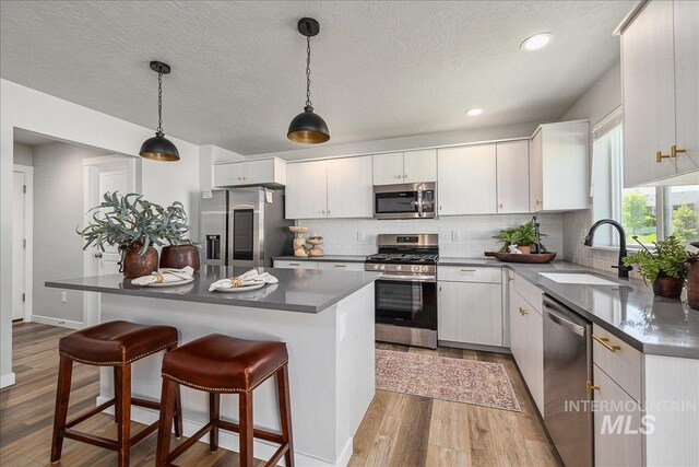 4849 N Willowside Ave, Meridian, ID 83646 - kitchen featuring stainless steel appliances, a sink, light wood-type flooring, dark countertops, and decorative backsplash