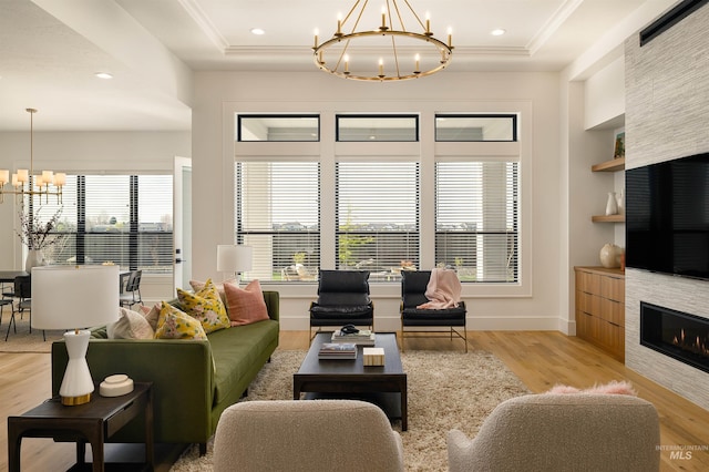 living room with an inviting chandelier, a tray ceiling, a tiled fireplace, and light wood-type flooring