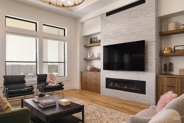 living room with built in features, a fireplace, ornamental molding, and light wood-type flooring