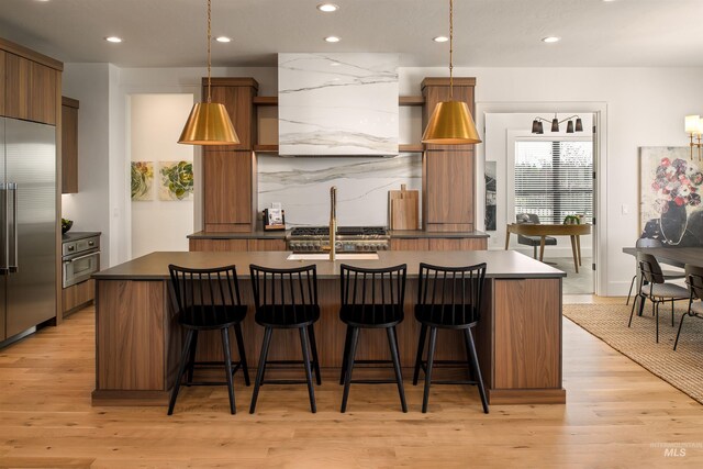 kitchen with appliances with stainless steel finishes, hanging light fixtures, a center island with sink, and light hardwood / wood-style floors