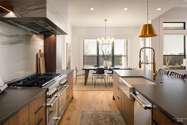 kitchen with decorative light fixtures, a notable chandelier, light hardwood / wood-style flooring, stainless steel appliances, and wall chimney exhaust hood