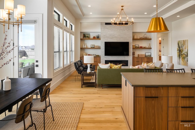 living room with a notable chandelier, a raised ceiling, a fireplace, light hardwood / wood-style flooring, and built in shelves