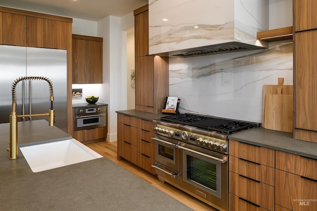 kitchen with premium appliances, tasteful backsplash, custom exhaust hood, and light wood-type flooring