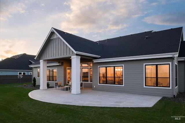 back house at dusk featuring a lawn and a patio